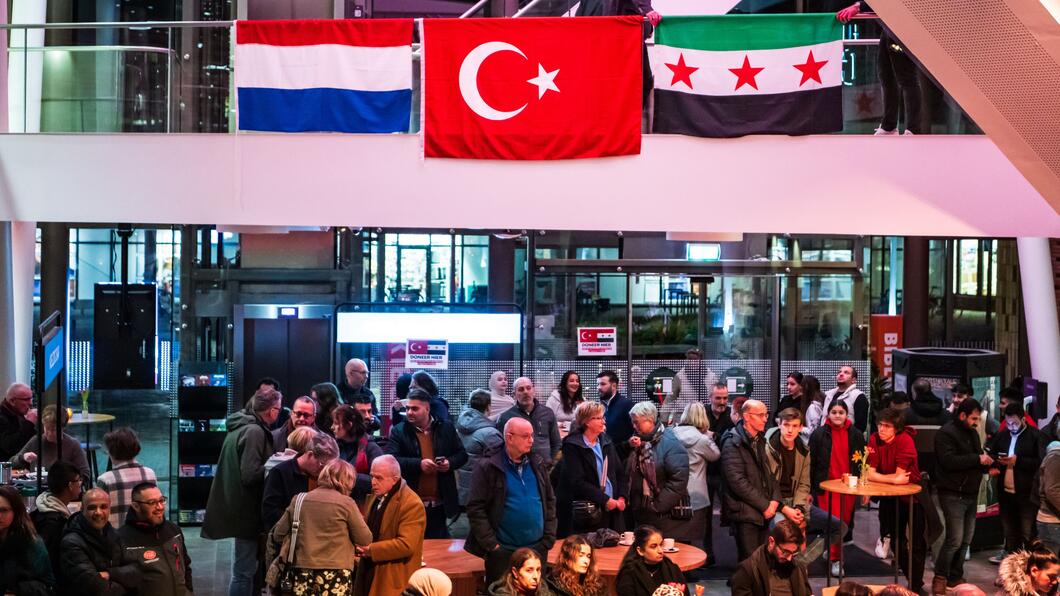 Drukke foyer met Nederlandse, Turkse en Syrische vlag