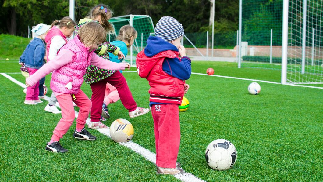 Afbeelding van kinderen op een voetbalveld. Ze spelen met ballen.