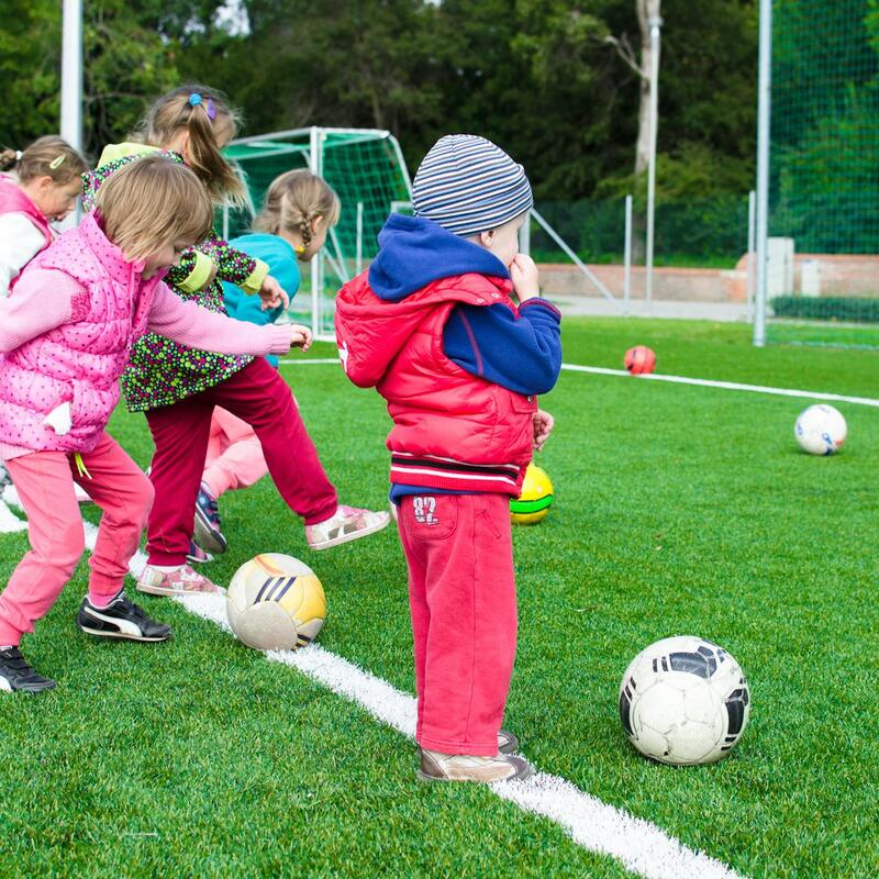 Afbeelding van kinderen op een voetbalveld. Ze spelen met ballen.